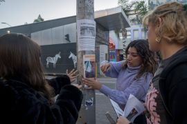 Three women gather around a utility pole in Tijuana, where they tape a missing persons poster.
