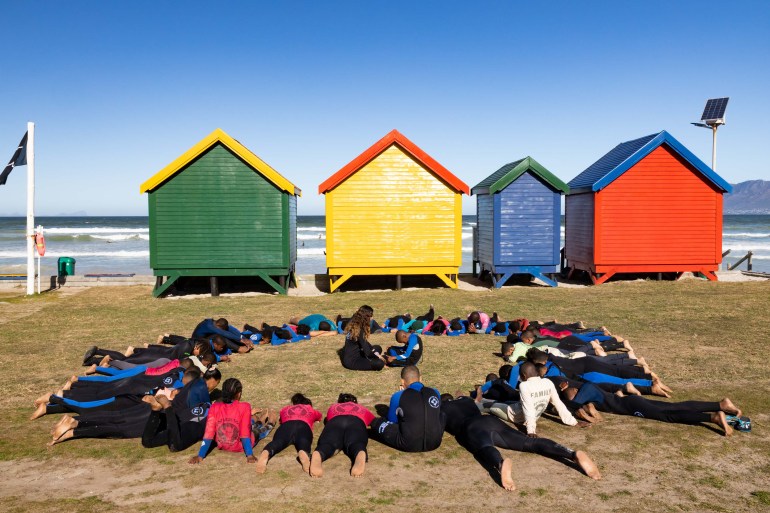 A sharing circle on the beach with colourful beach huts and the sae in the background