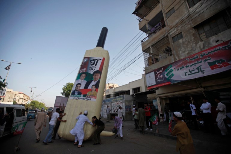 Supporters of Imran Khan, Pakistani cricketer-turned-politician and chairman of political party Pakistan Tehreek-e-Insaf (PTI), install a giant bat symbol along a roadside in Karachi.