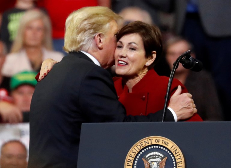 Donald Trump embraces Kim Reynolds as she stands behind a podium emblazoned with the presidential seal.