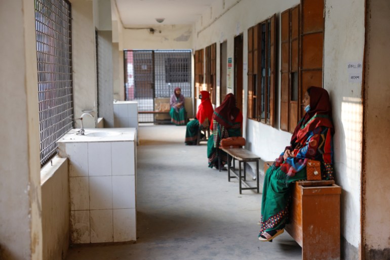 Election officials sitting around as they wait for voters in a polling station in Dhaka. There are four women seated on benches along a corridor. One is sitting on a cupboard