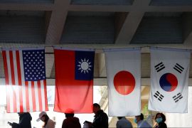 People in Taiwan queuing to vote beneath the flags of the US, Taiwan, Japan and South Korea