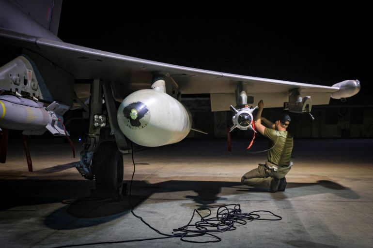 A weapons technician squatting beneath the wing of an RAF typhoon ahead of attacks on Houthi targets in Yemen