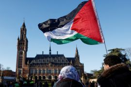 Protesters hold a Palestinian flag as they gather outside the International Court of Justice (ICJ)