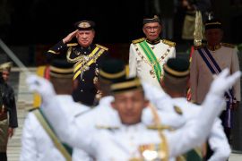Sultan Ibrahim Sultan Iskandar salutes the guard of honour, beside Malaysia's Prime Minister Anwar Ibrahim at the National Palace. They are both in ceremonial uniforms/ Sultan Ibrahim's is black and Anwar's white with a green sash.