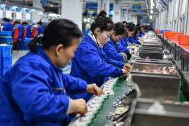 Women working on a production line at an electronics factory in Anhui province. They are all wearing blue jackets and their hair is tied back.