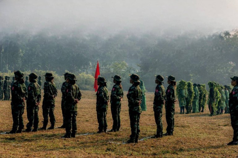 Women fighters from the Dawei district PDF. They are standing in formation in an open area. There is a red flag.