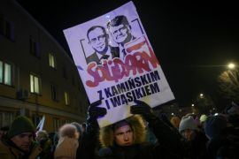 A protester holds a sign with effigies of detained former MPs Mariusz Kaminski and Maciej Wasik near the Grochow police station