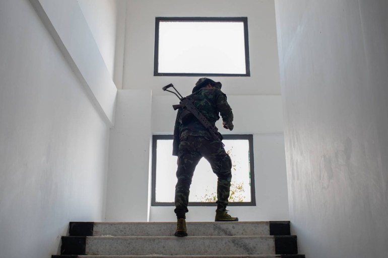 A fighter from the Karenni resistance forces walking up stairs in a building captured from the military. He is armed and is silhouetted against the window