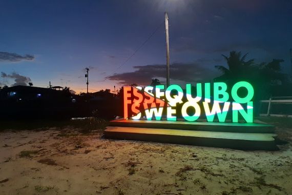 An electric sign, lit up with the colours of the Guyanese flag, says: "Essequibo is we own." Behind the sign is the faint glow of daylight.