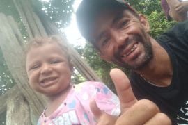 Emiliannys — a little girl in a pink T-shirt — and her father Victor Hidalgo Lopez, who wears a ballcap and flashes a thumbs-up at the camera.