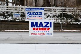 Yard signs for Mazi Pilip and Tom Suozzi sit planted in the snow beside a Long Island road.