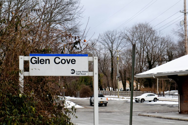 A sign reading "Glen Cove" stands beside a parking lot and road after a fresh snow.