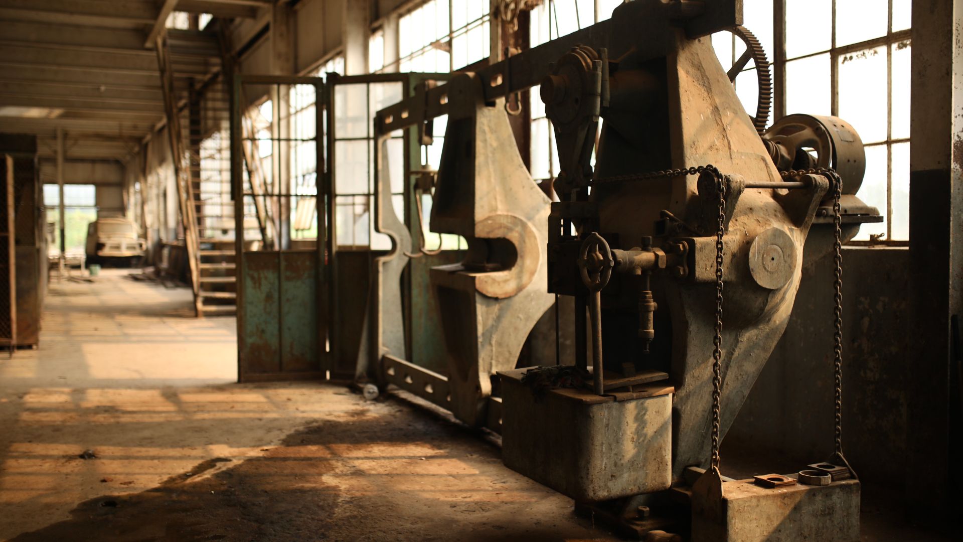 Heavy machinery sits rusted on an old factory floor.