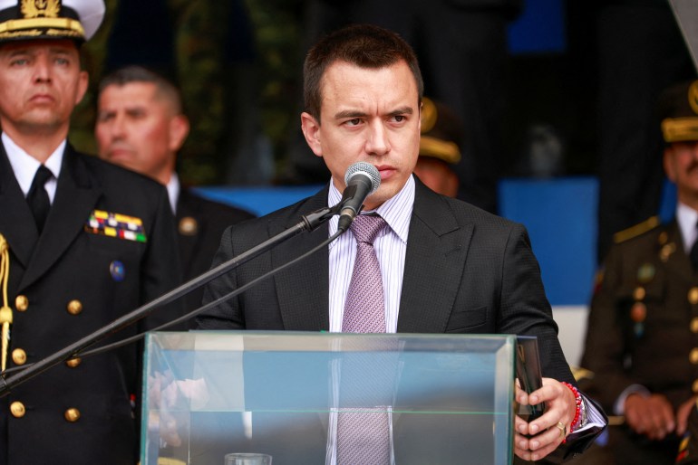 Daniel Noboa, in a suit and tie, stands behind a glass podium, with brows furrowed.