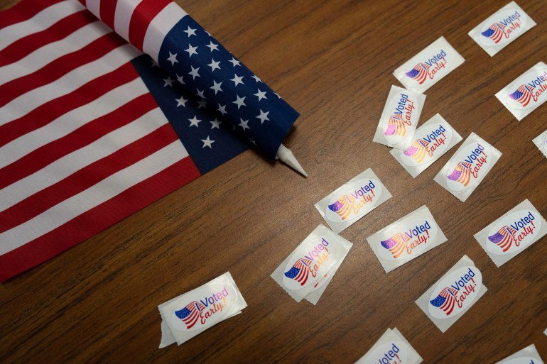 An American flag sits on a wooden table next to "I voted" stickers.