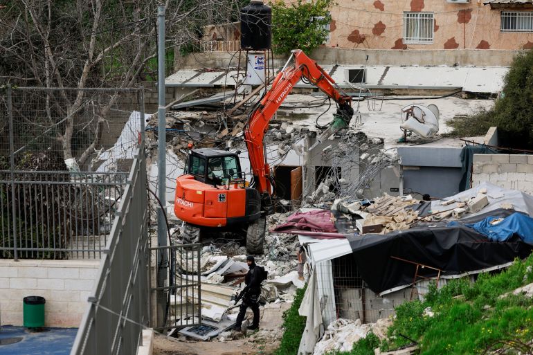 An Israeli border policeman stands by as a bulldozer demolishes the house of a Palestinian family in Silwan in East Jerusalem, February 14