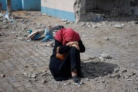 A woman rests next to a damaged building, as Palestinian arrive in Rafah after they were evacuated from Nasser hospital