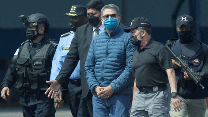 Juan Orlando Hernandez, wearing a face mask and sunglasses, walks in the custody of US federal agents.