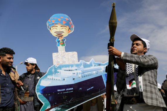 A Houthi follower holds a rocket launcher as others carry a cutout banner, portraying the Galaxy Leader cargo ship which was seized by Houthis, during a parade as part of a 'popular army' mobilization campaign by the movement, in Sanaa, Yemen, February 7, 2024