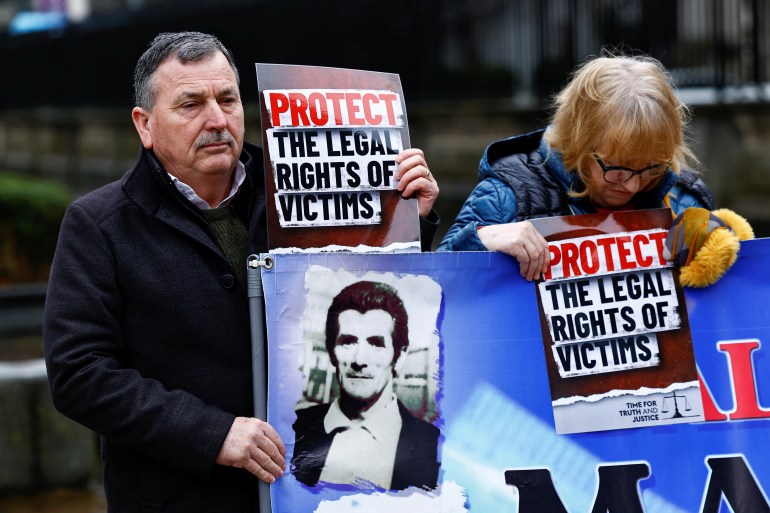 John Teggart, the son of Daniel Teggart who was killed during the Ballymurphy massacre in Belfast in 1971, holds a sign and a banner, in support of relatives and victims of the conflict known as 'The Troubles' in Northern Ireland, at the Royal Courts of Justice ahead of a High Court judgment in a landmark legal challenge to the UK government's Troubles Legacy Act, in Belfast, Northern Ireland, February 28, 2024. REUTERS/Clodagh Kilcoyne