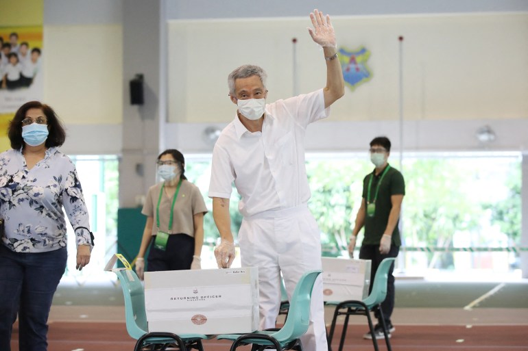Singapore Prime Minister Lee Hsien Loong voting. He is waving to photographers. The ballot box is on two plastic chairs.