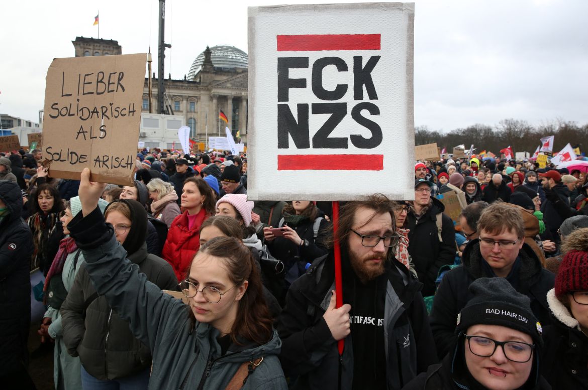 Demonstrators hold up placards reading 'Rather to show solidarity instead of being solid Aryan' and 'Fuck Nazis' as they protest during a rally under the motto 'We are the firewall' called for by international non-profit organisation 'Hand in Hand' against right-wing politics in front of the Reichstag building in Berlin, Germany on February 3