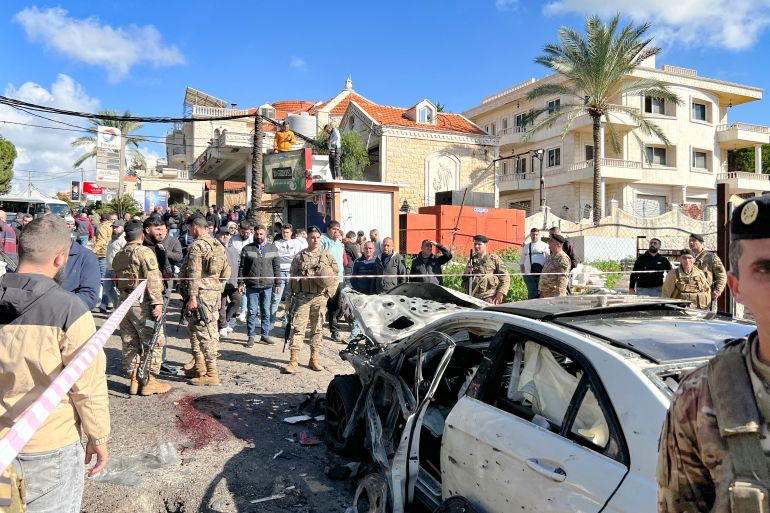 Blood stains cover the ground next to a a car wrecked in a reported Israeli drone attack, as Lebanese army soldiers secure the area in the village of Jadra between Beirut and the southern city of Sidon