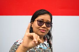 An Indonesian woman shows her ink-stained finger after casting her vote. She is stranding in front of the red and white of an Indonesian flag