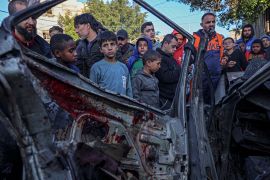 Onlookers gather around a car that was destroyed in an Israeli raid in Rafah in the southern Gaza Strip [Said Khatib/AFP]