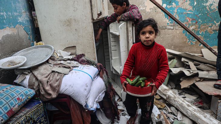 A child carries food items as another tries to salvage more from a refrigerator inside their damaged home, following overnight Israeli bombardment in Rafah in the southern Gaza Strip on February 25