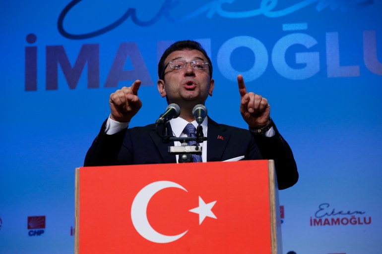 Ekrem Imamoglu gestures as he delivers a speech against a blue background