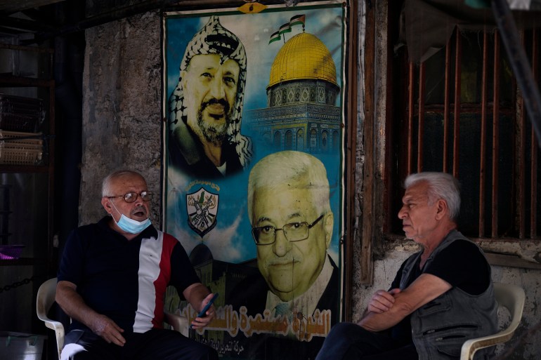 Palestinians speak as they sit next to a poster of the late Palestinian leader Yasser Arafat, left, and Palestinian President Mahmoud Abbas, right, at the Bourj al-Barajneh Palestinian refugee camp, in Beirut, Lebanon, Friday, Oct. 21, 2022. Lebanon's historic economic meltdown is hard hitting Palestinian refugees in the small nation where the vast majority of them now live in poverty while others risk their lives in search for a better future abroad, the U.N. agency for Palestinian refugees said Friday. (AP Photo/Bilal Hussein)