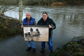 Billy Frank Jr and Ed Johnstone together hold an enlarged photo showing Indigenous ancestors fishing in the 1960s and 1970s where they are standing now.