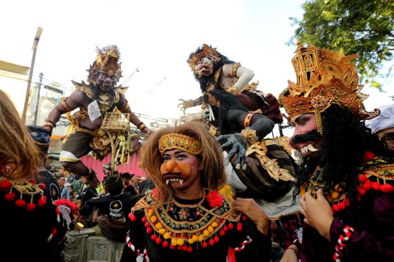 Balinese dancers in traditional costumes in front of ogoh-ogoh effigies. The giant statues represent evil spirits