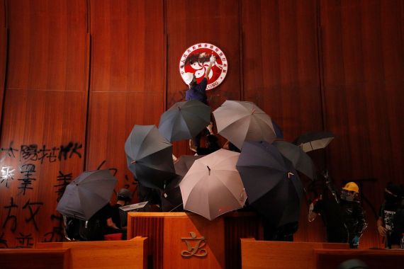 Protesters daub the Hong Kong emblem inside the chamber of the Legislative Council. They are holding up umbrellas.