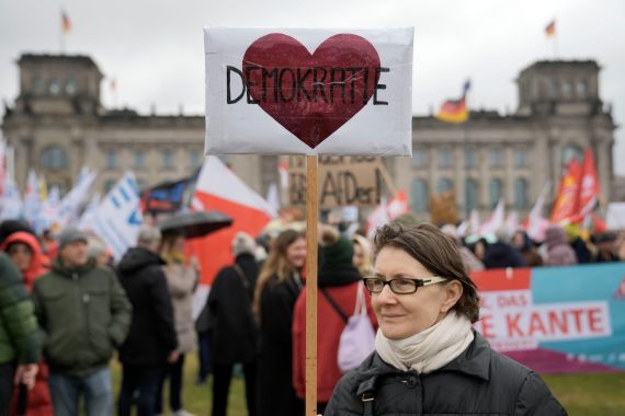 A protestor holds a sign reading 'Democracy' in front of Germany's parliament Reichstag during a demonstration against the AfD party and right-wing extremism in Berlin, Germany, Saturday, Feb. 3
