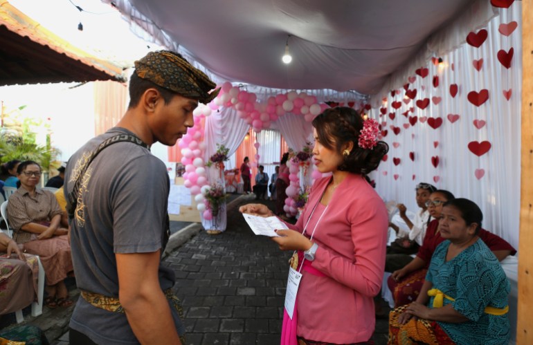 A man waits for his turn to vote at a Valentine's themed polling station in Bali. There are garlands of red hearts hanging on the wall and pink ballooons and ribbons