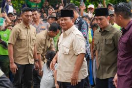 Prabowo Subianto. He is dressed in a pale coloured shirt with a black songkok. There is security around him