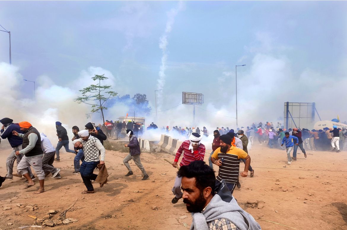 Farmers run for cover after police fired tear gas to disperse protesting farmers who were marching to New Delhi near the Punjab-Haryana border at Shambhu, India, Tuesday, Feb.13