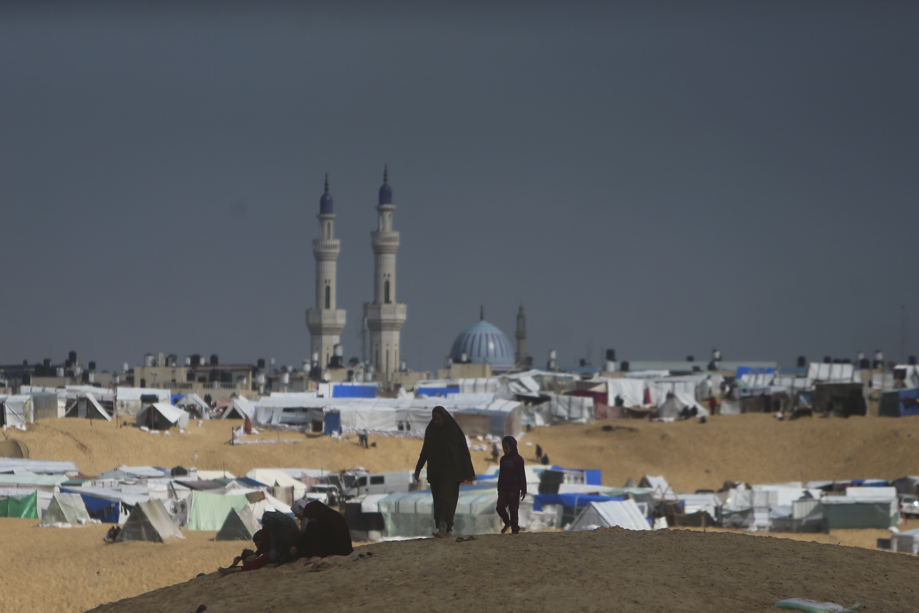 Palestinians displaced by the Israeli ground offensive on the Gaza Strip walk at the makeshift tent camp in Rafah, Gaza Strip, Sunday, Feb. 18