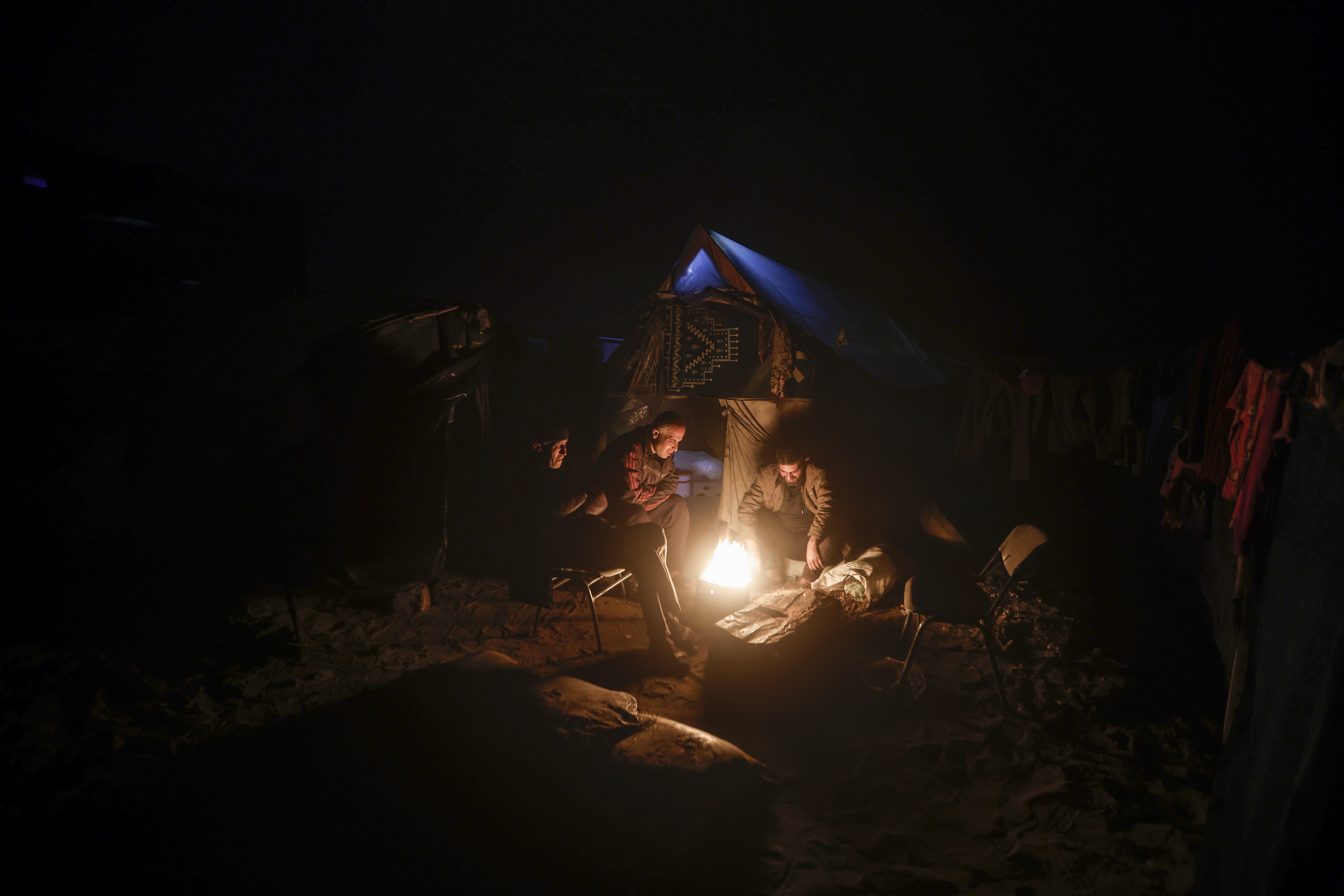 Palestinians displaced by the Israeli ground offensive on the Gaza Strip sit by a fire at a makeshift tent camp in Rafah, Gaza Strip, Sunday, Feb. 18