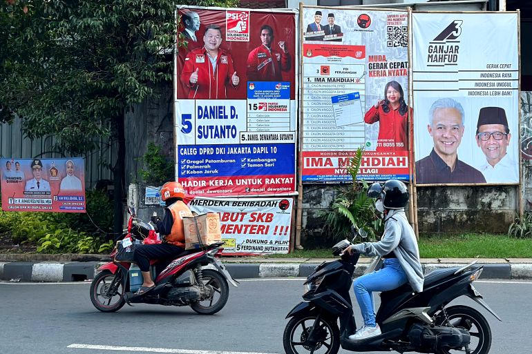 Motorcyclists drive past campaign banners for various candidates in Jakarta