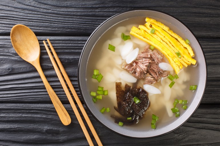 Tteokguk or sliced rice cake soup is a traditional Korean dish eaten during the celebration of the Korean New Year closeup in the bowl on the table.