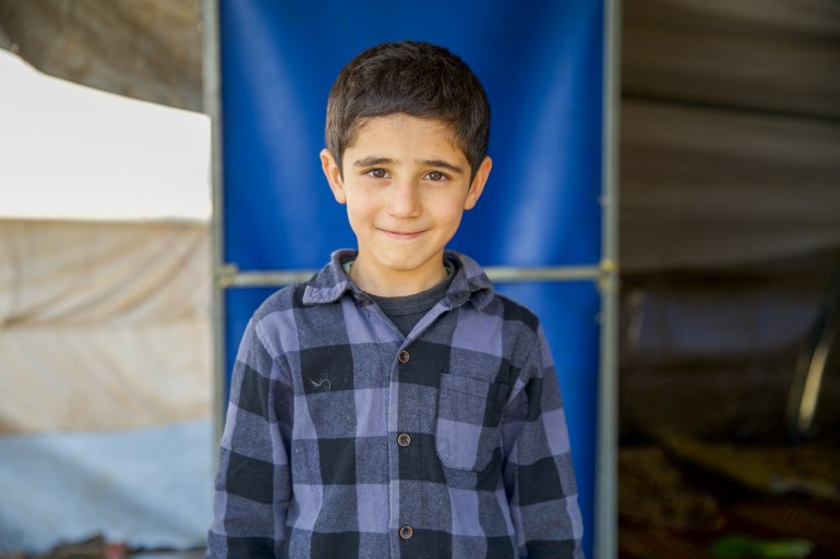 Hussein stands smiling in a blue plaid shirt