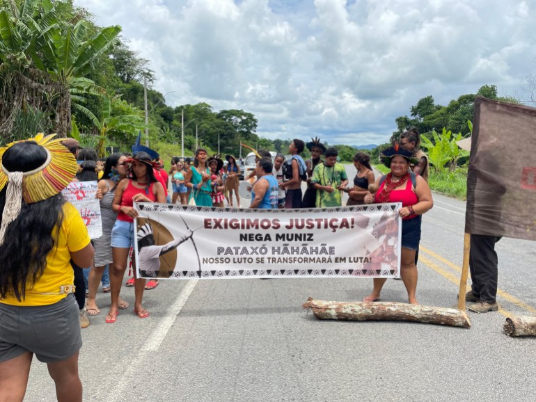 Protesters hold up a banner and stand in the roadway to call for justice in the shooting death of an Indigenous leader.