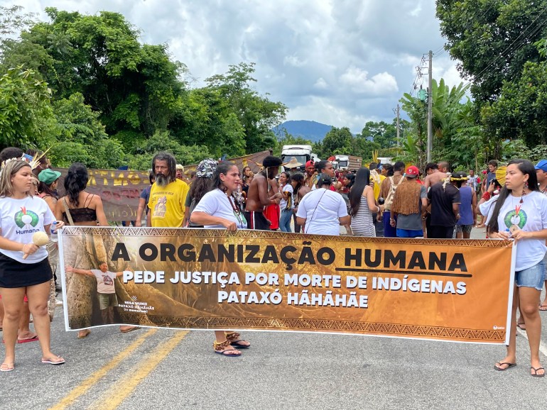 Protesters on a roadway in Brazil hold up a banner calling for justice in the case of a late Indigenous leader shot to death.