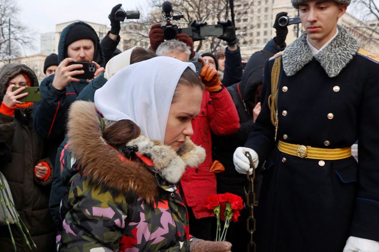 Woman holding red roses in protest in front of Russian guard.