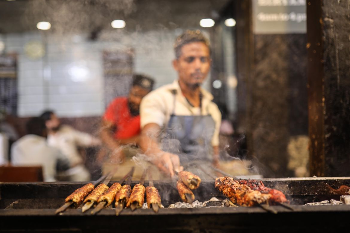 A chef arranges kebab rods on a grill. [Meer Faisal/Al Jazeera]