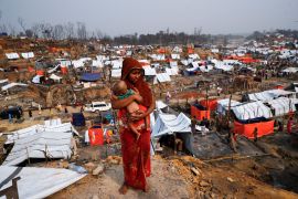 A Rohingya refugee woman carries her child as she looks on in a refugee camp